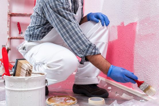 recorte de pintor agachado imprimiendo pintura blanca sobre pared rosa